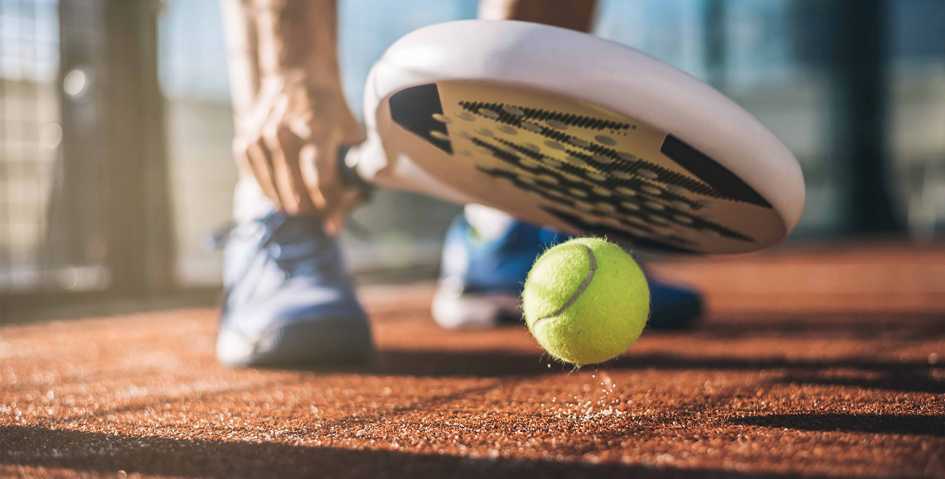 Homme ramassant une balle avec sa raquette de padel